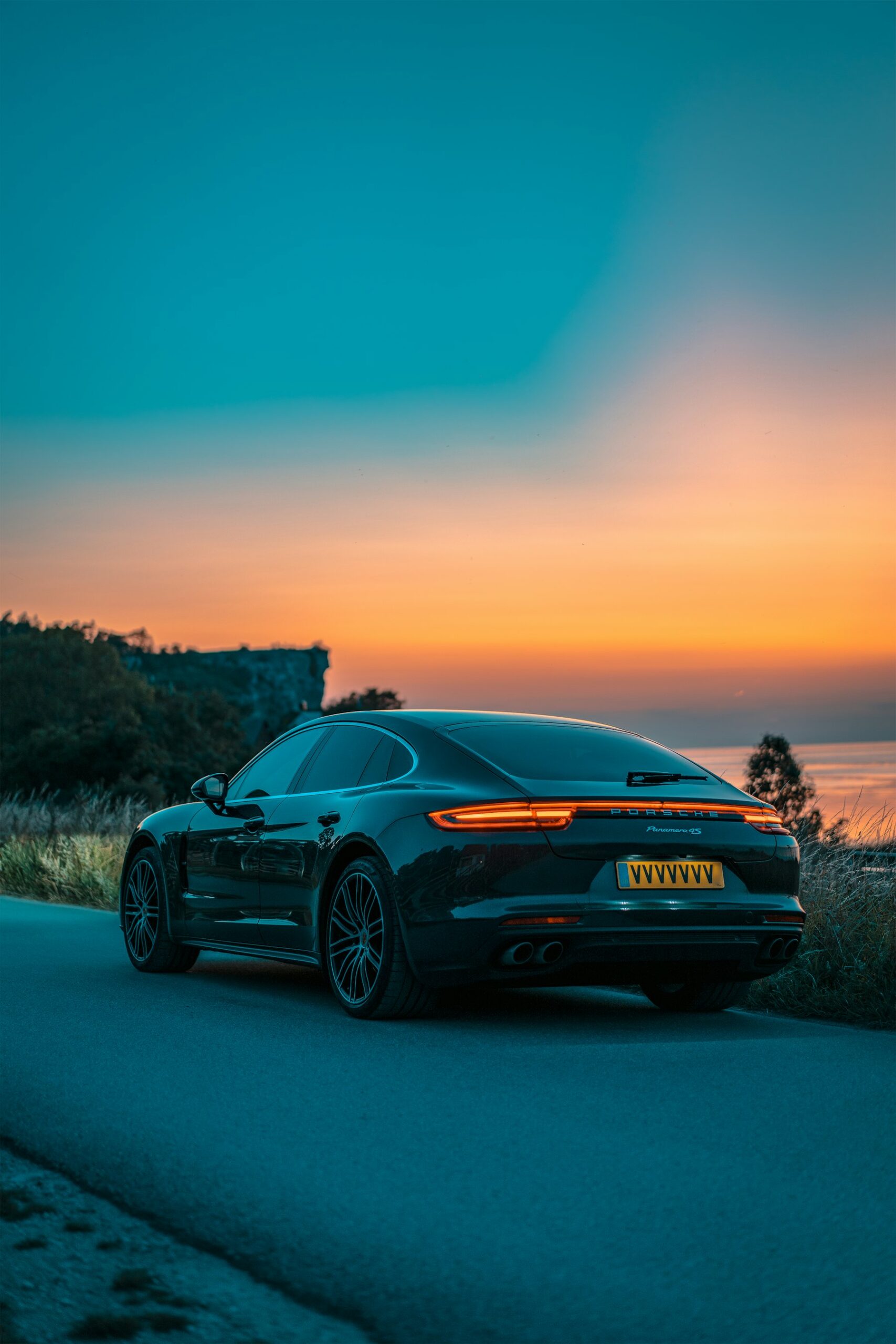 Black Porsche Panamera with tinted windows on a coastal road at sunset
