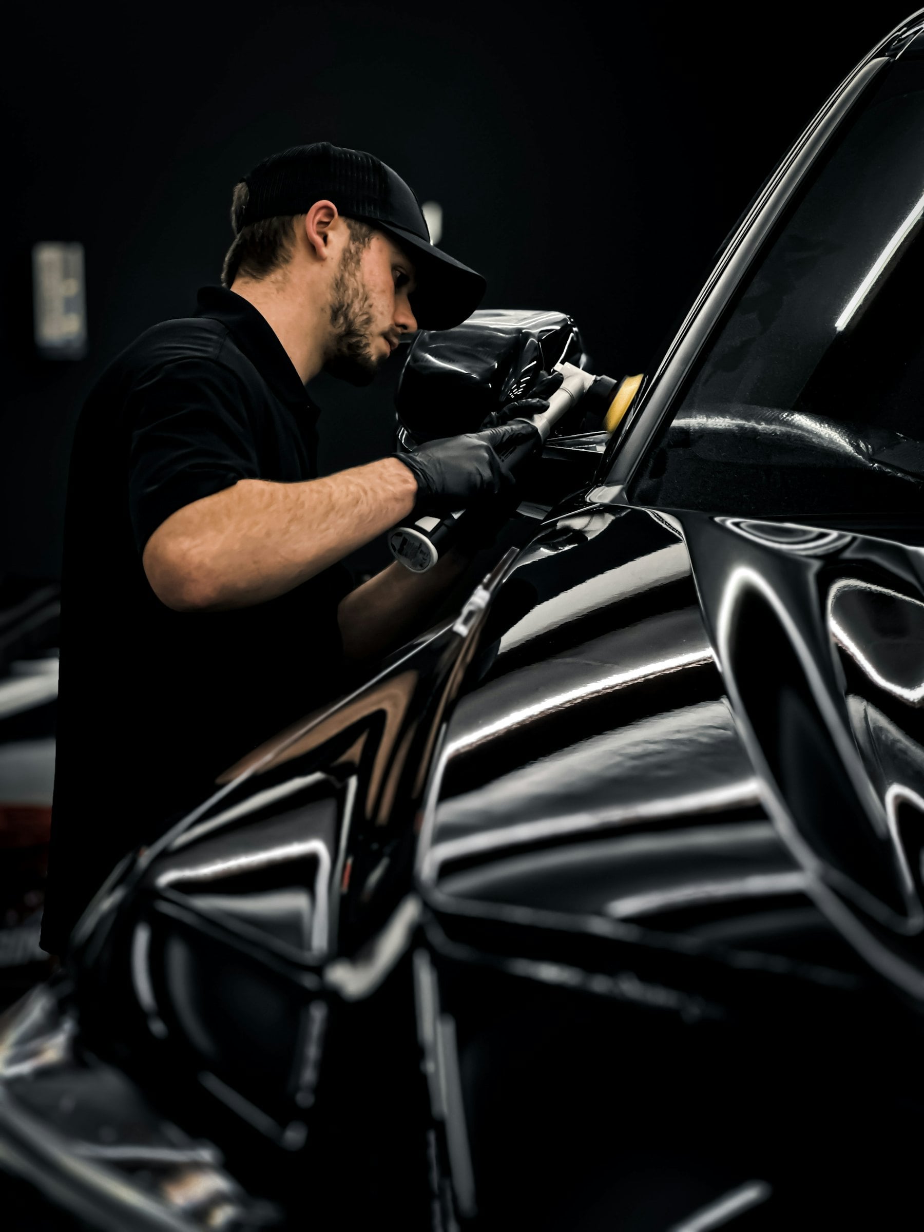 Technician in black gloves installing paint protection film on a black car